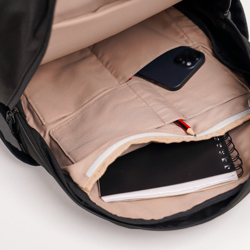an open luxe backpack in black, inside the bag there is a notepad, iphone and pencil.