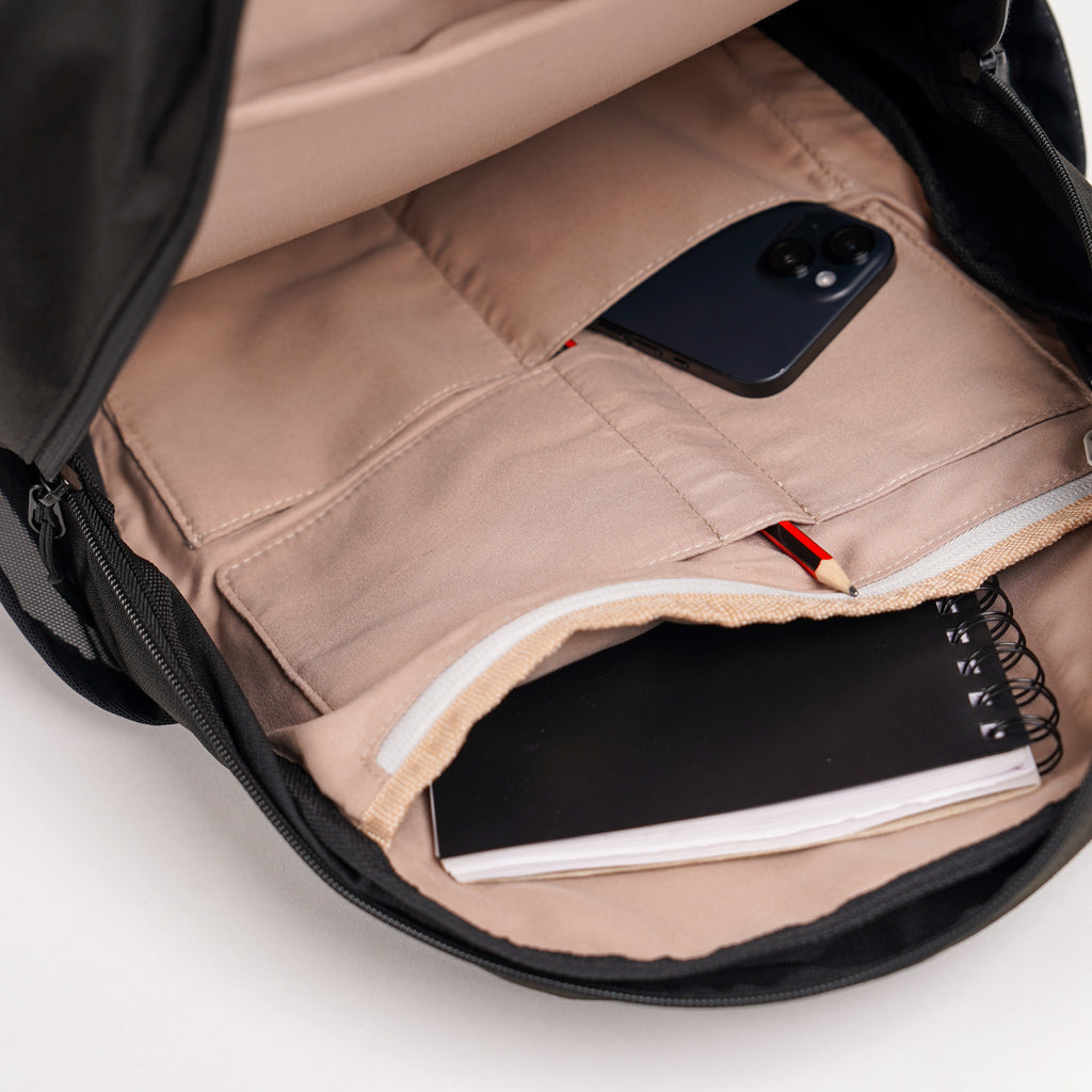 an open luxe backpack in black, inside the bag there is a notepad, iphone and pencil.