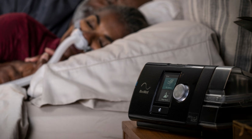 Person sleeping comfortably with a ResMed CPAP nasal mask, with ResMed AirSense 10 machine on the bedside table.