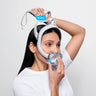 Woman is putting on the F30i, she is standing to the side. pulling the front first and the back of the mask second