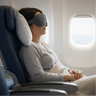 woman on the plane, she has a pillow under her neck and head, wearing an nyx mask while traveling.