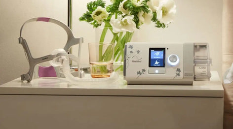 CPAP machine on a nightstand with flowers and a mask